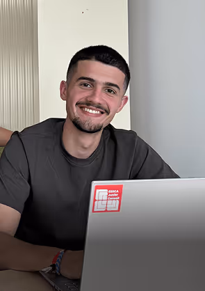 Jeune homme souriant assis devant un ordinateur portable avec un autocollant rouge.