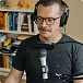 Homme portant des lunettes et un casque, parlant devant un microphone en studio.
