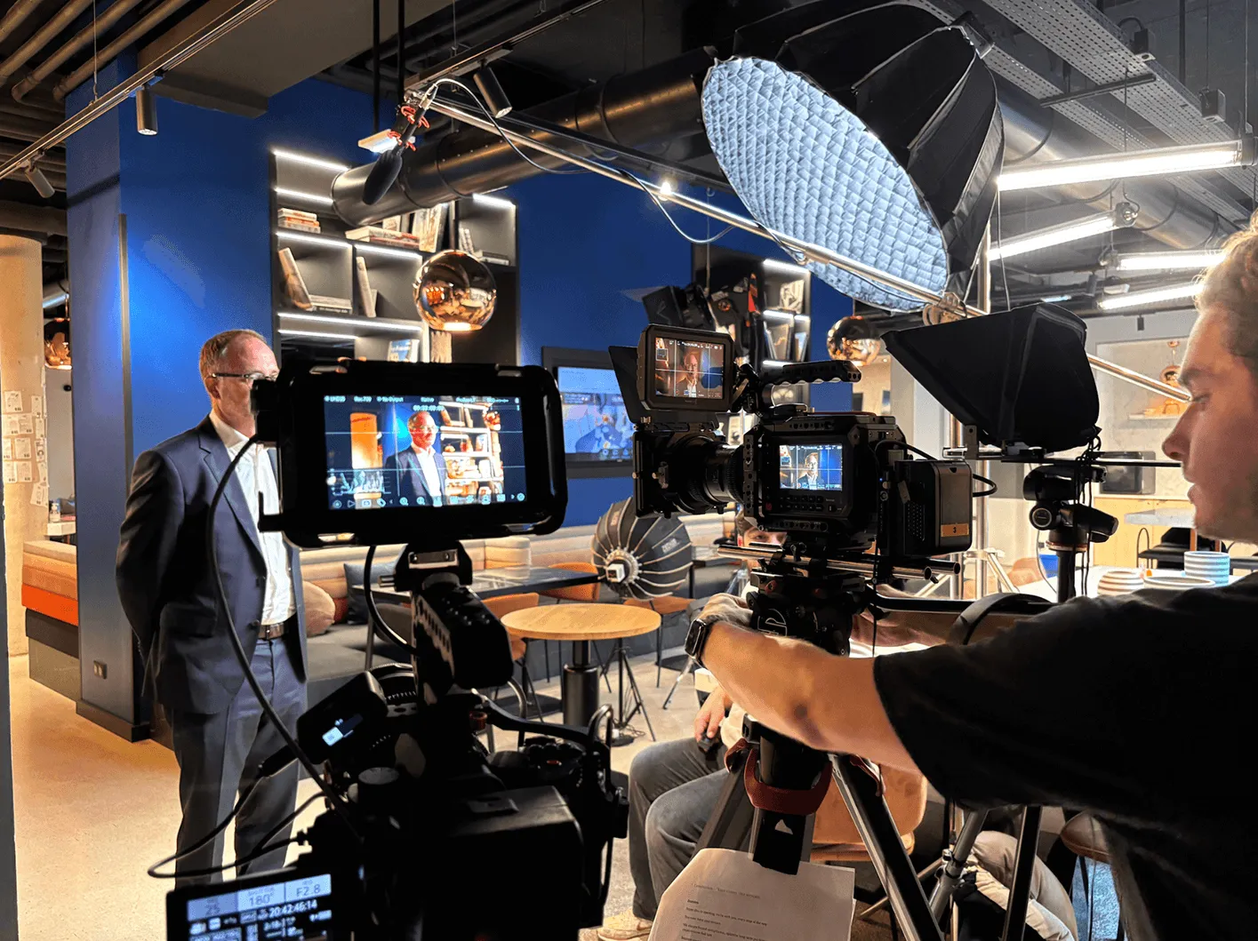 Tournage d'une interview en studio avec un homme en costume, plusieurs caméras et éclairages professionnels.
