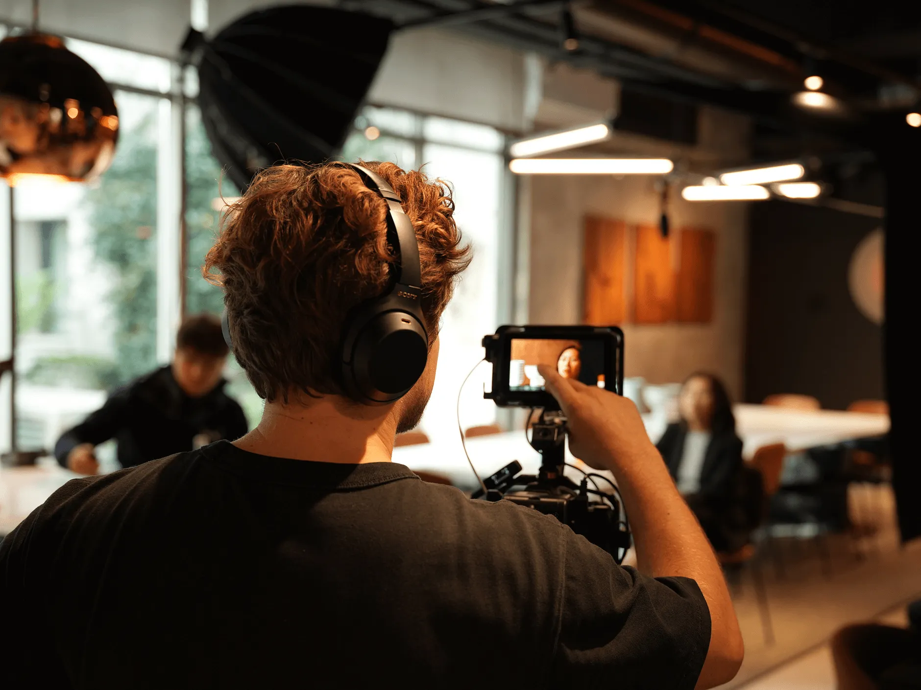 Un homme portant un casque règle une caméra lors d'un tournage en studio avec une femme assise en arrière-plan.