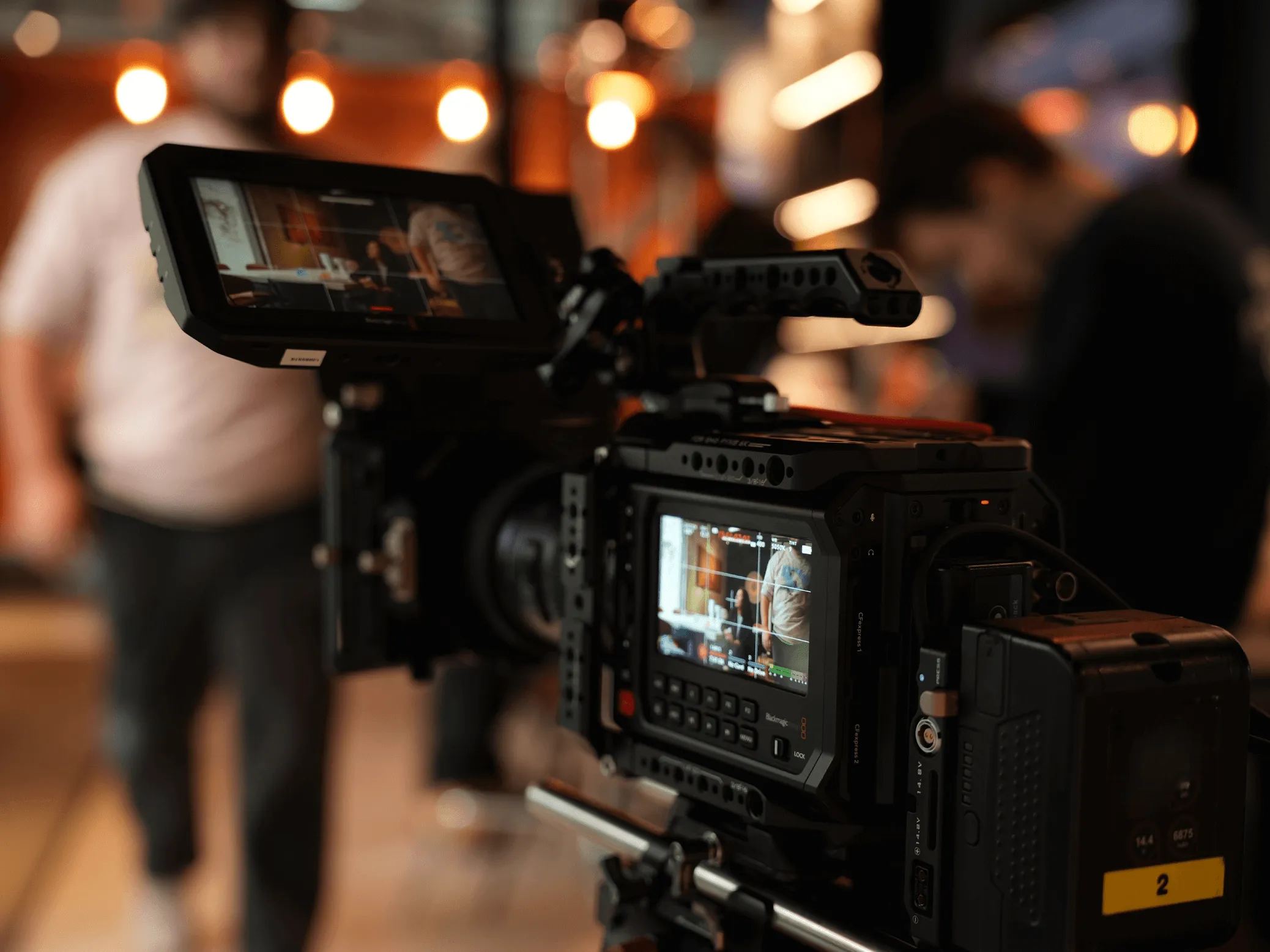 Caméra vidéo professionnelle avec écran d'affichage montrant une scène floue de personnes en arrière-plan dans un studio lumineux.