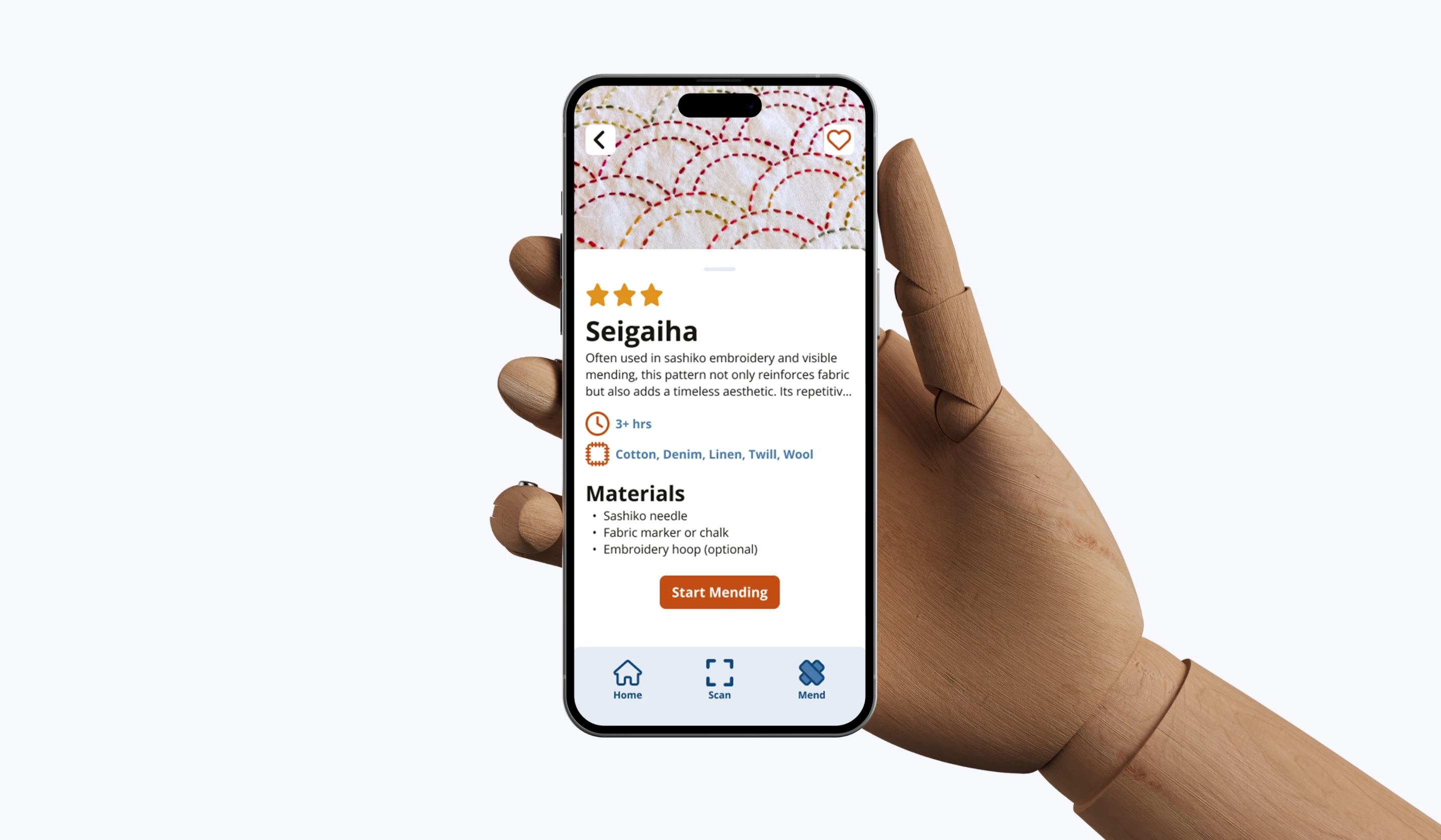 Wooden mannequin hand holding a smartphone displaying a sewing app with details about the Seigaiha stitching pattern, materials, and a start mending button.