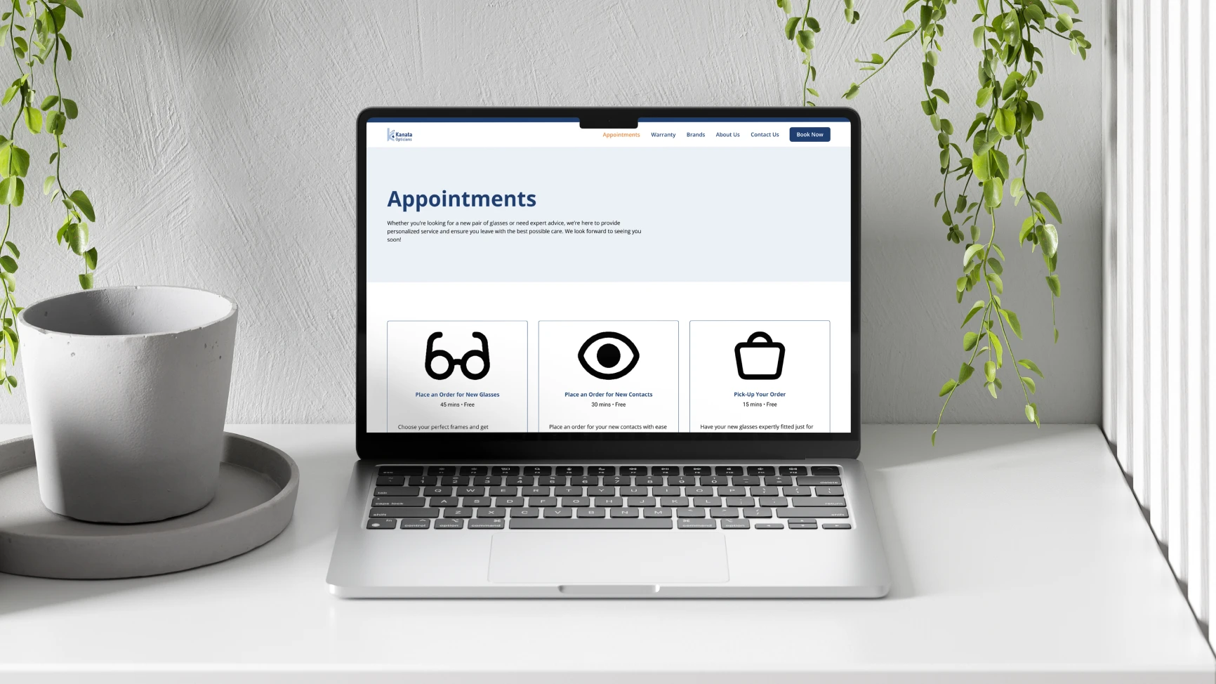 Laptop on white desk displaying an optician appointment booking webpage with icons for glasses, contacts, and order pickup.