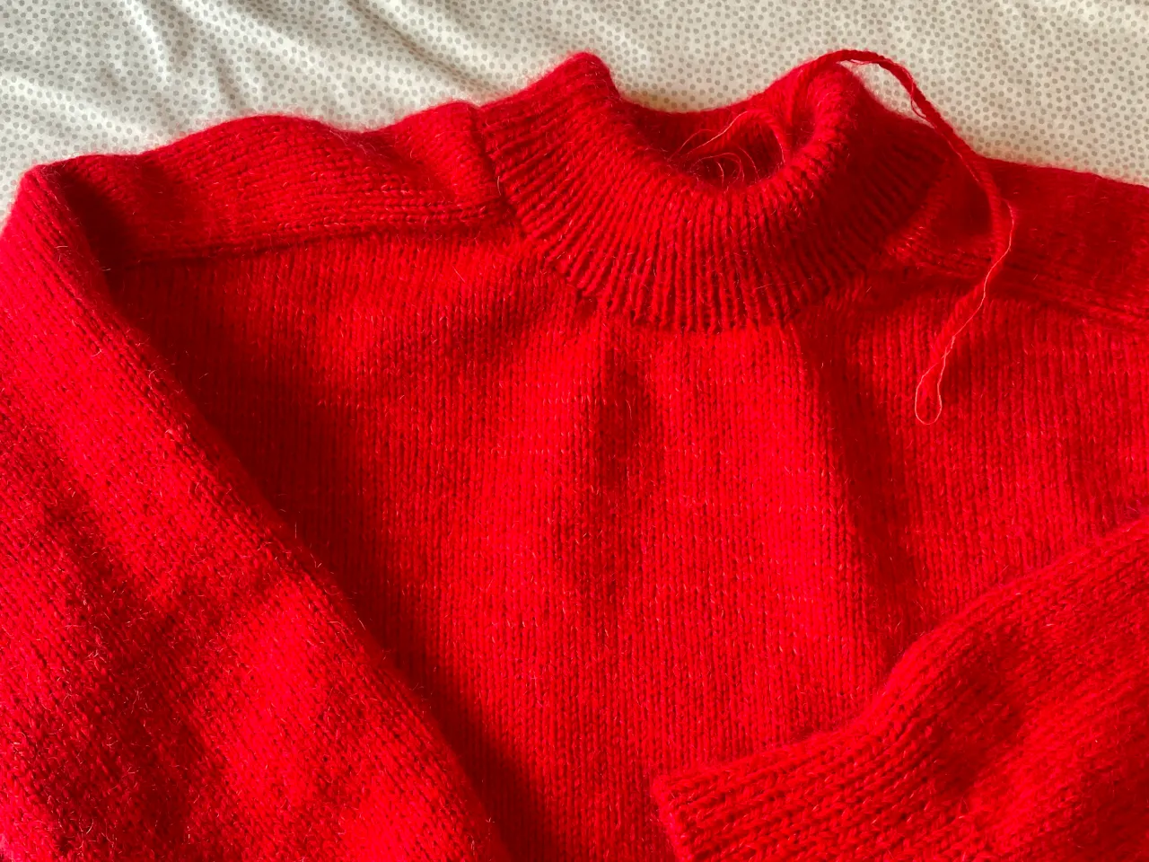 Bright red knitted sweater with a ribbed high neckline and long sleeves lying flat on a patterned fabric surface.