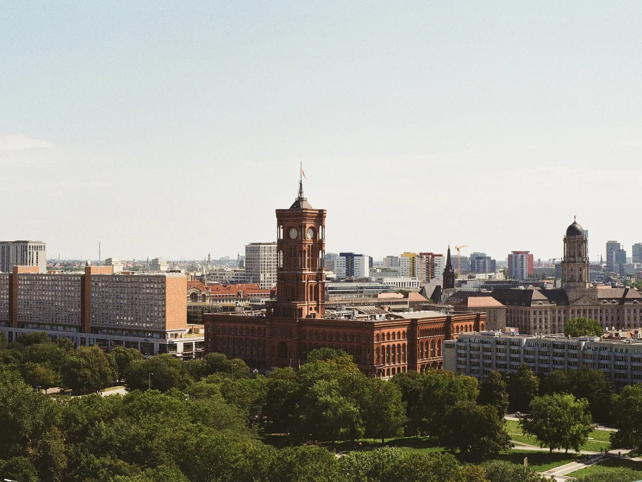 Cityscape with historic red brick building featuring a tall clock tower surrounded by modern buildings and green trees.