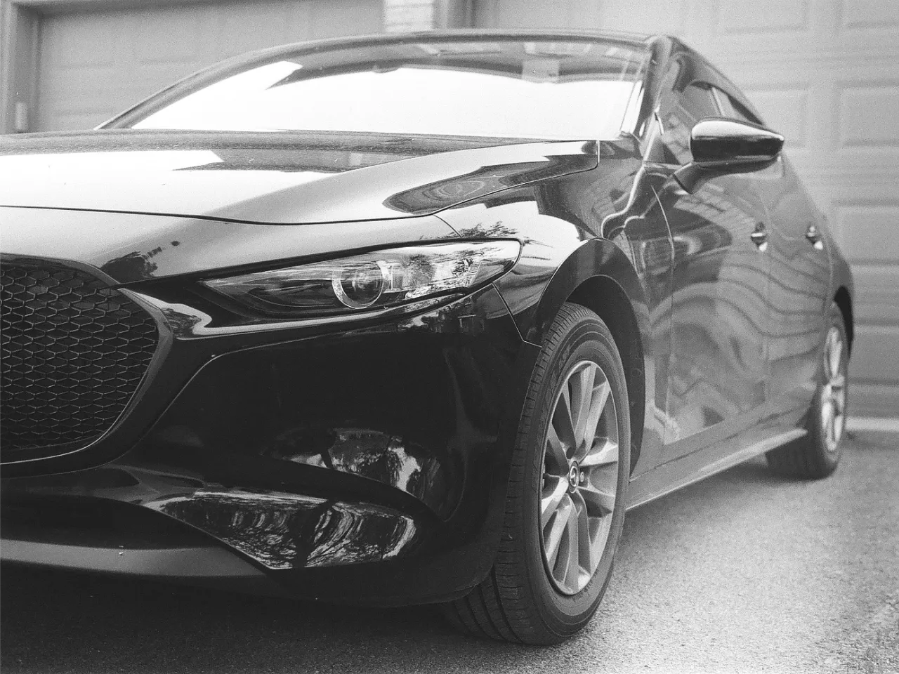 Front side view of a sleek modern car parked on a driveway with visible headlight and wheel.