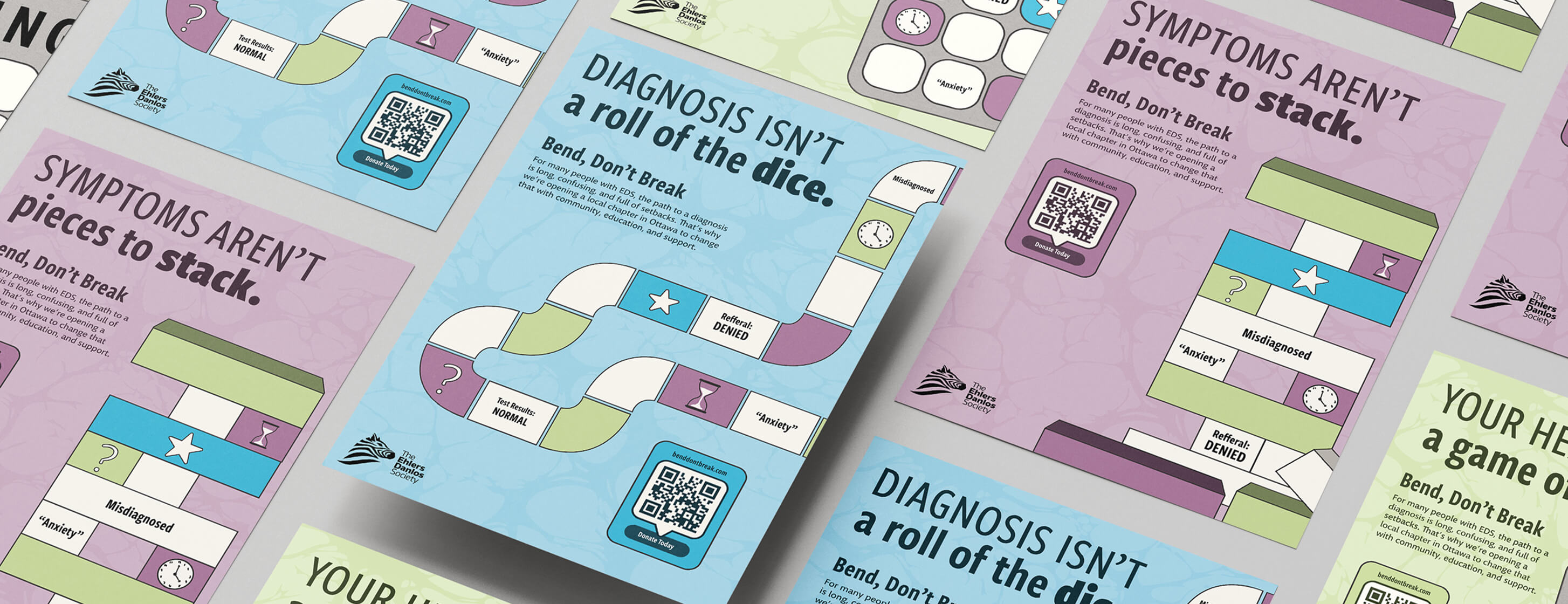 Overhead view of colorful awareness posters with board game illustrations highlighting challenges in EDS diagnosis and symptoms, featuring phrases like 'Symptoms aren't pieces to stack' and 'diagnosis isn't a roll of the dice,' with QR codes for donations.