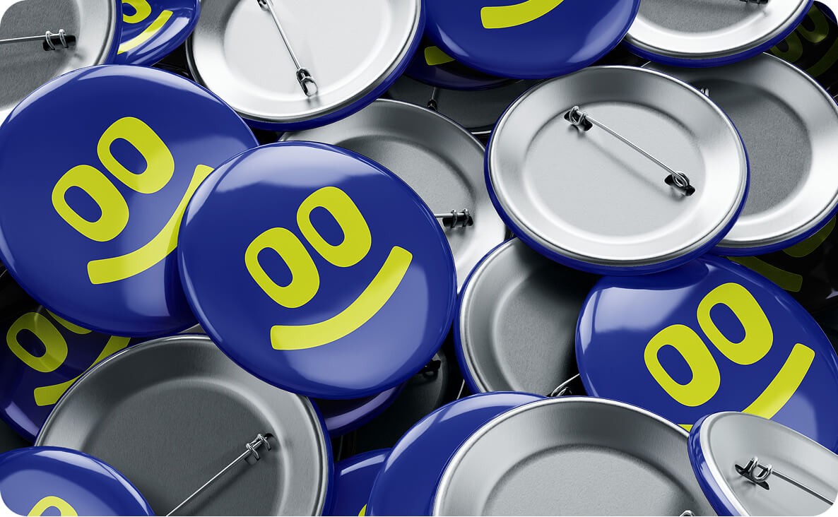 Cluster of blue round pin-back buttons with a green smiley face featuring two oval eyes and a curved mouth.