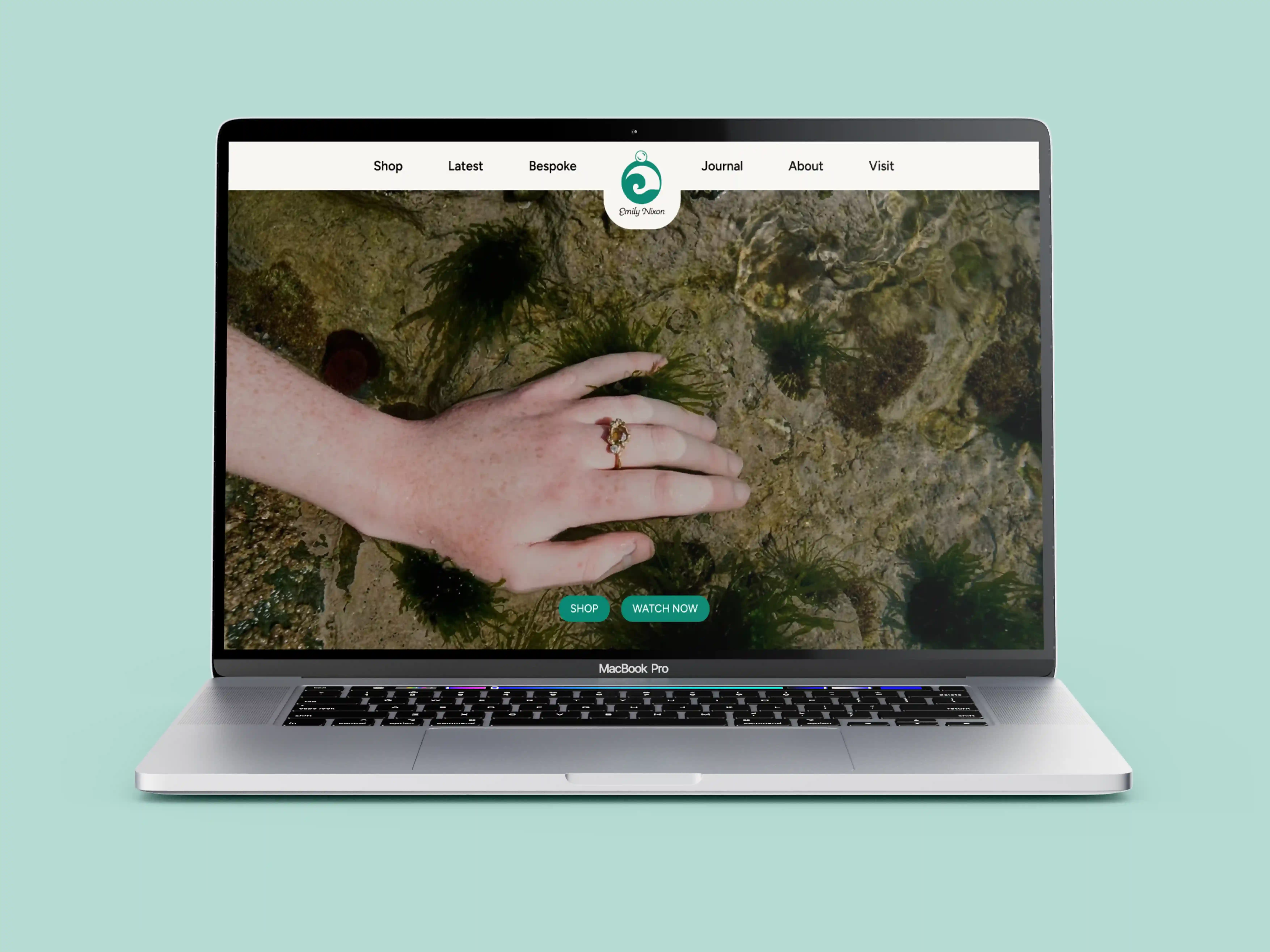 MacBook Pro displaying a website with a hand wearing a decorative ring touching underwater plants.