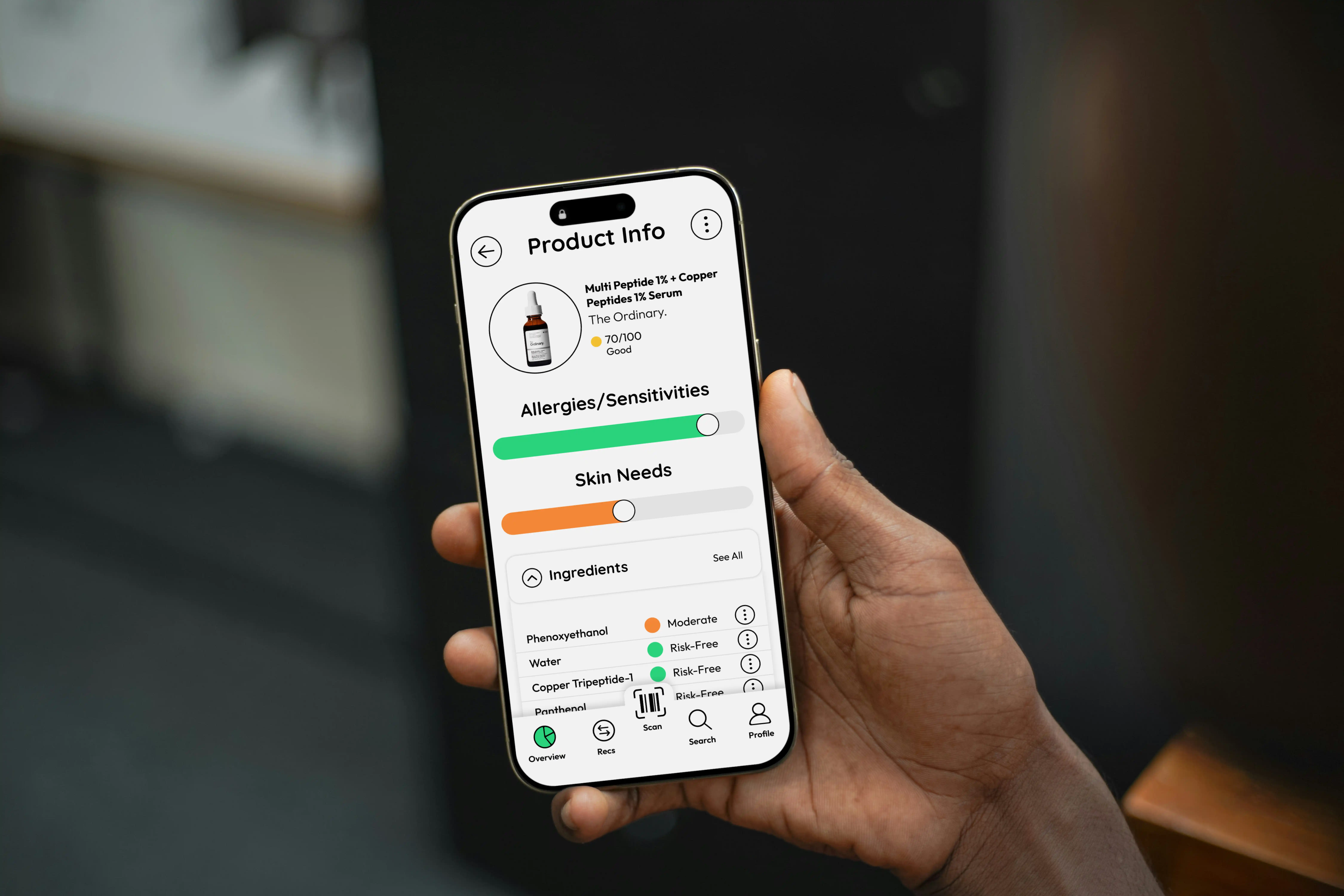 Hand holding smartphone displaying product info for The Ordinary Multi Peptide 1% + Copper Peptides 1% Serum with allergy and skin needs sliders and ingredient risk levels.