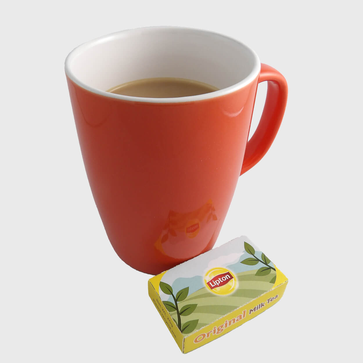 Orange mug filled with milk tea beside a Lipton Original Milk Tea packet.
