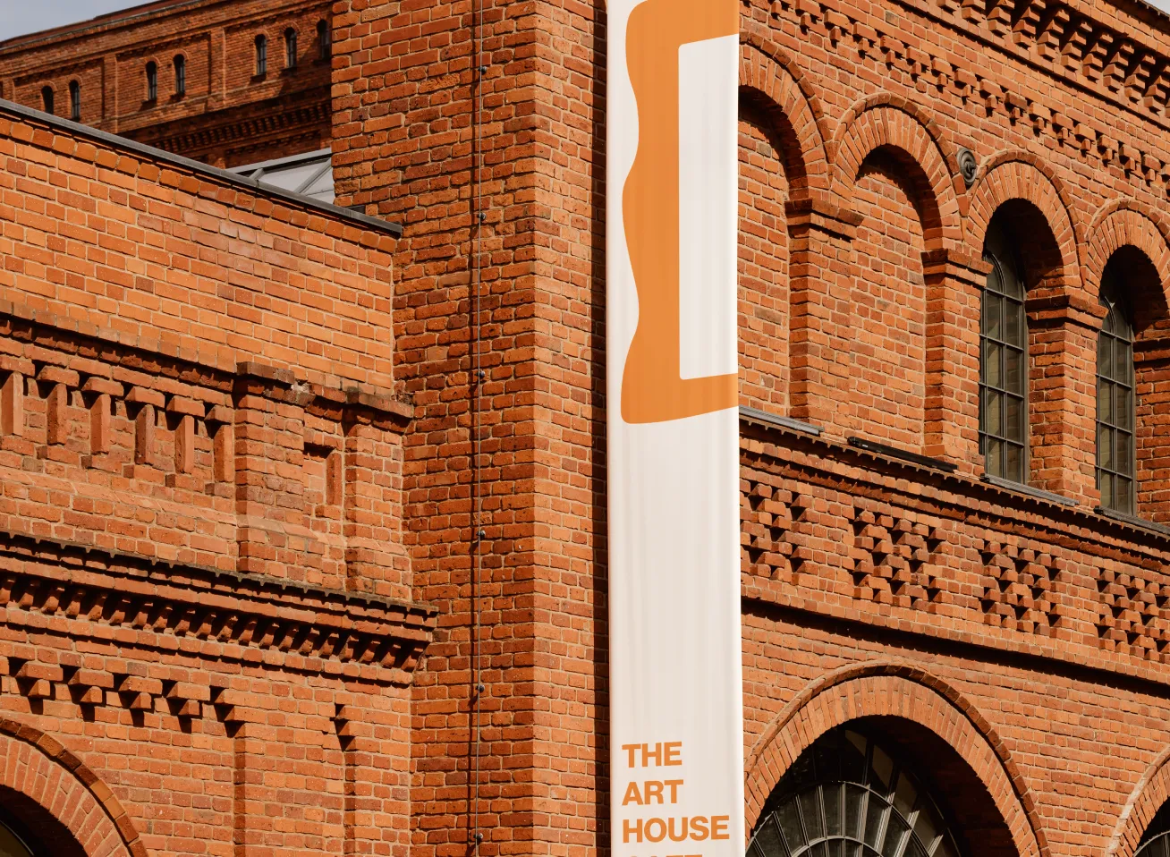 Close-up view of red brick building facade with arched windows and decorative brickwork, featuring a vertical banner reading 'THE ART HOUSE'.