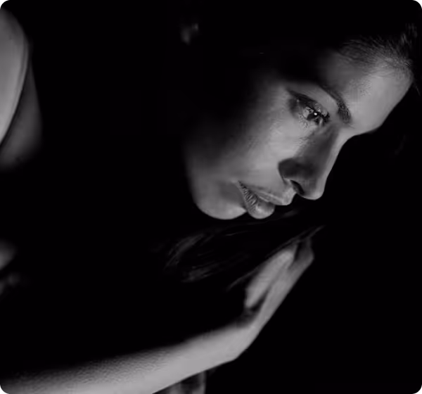 Black and white close-up of a woman lying down with a tear on her cheek against a dark background.
