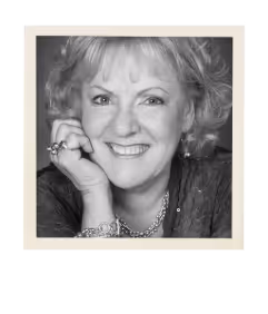 Black and white portrait of a smiling older woman resting her chin on her hand, wearing rings and a necklace.