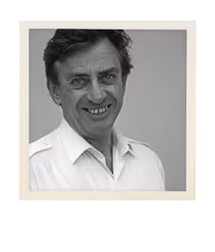 Black and white portrait of a smiling middle-aged man with dark hair wearing a white collared shirt.