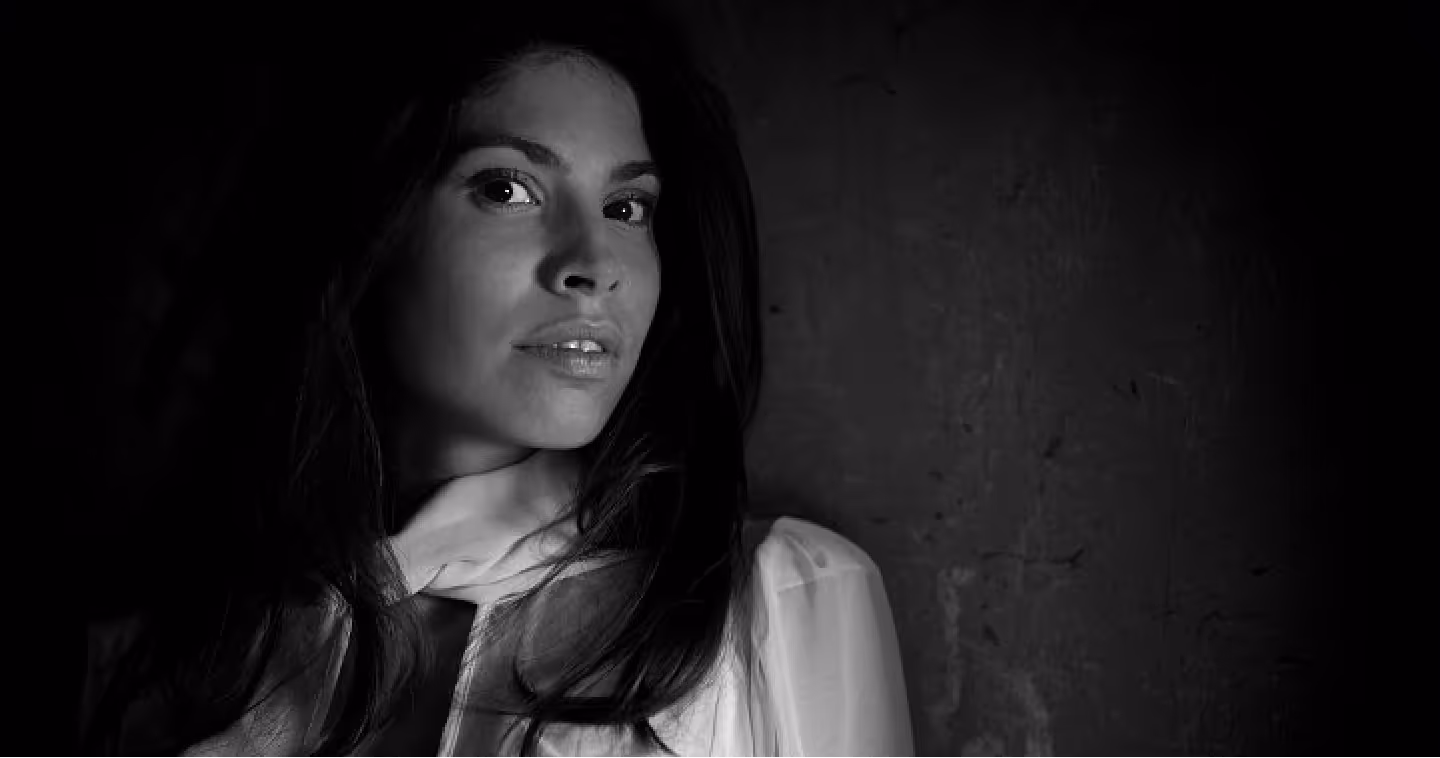Black and white portrait of a woman with long dark hair wearing a light-colored scarf and blouse, looking slightly to the side.