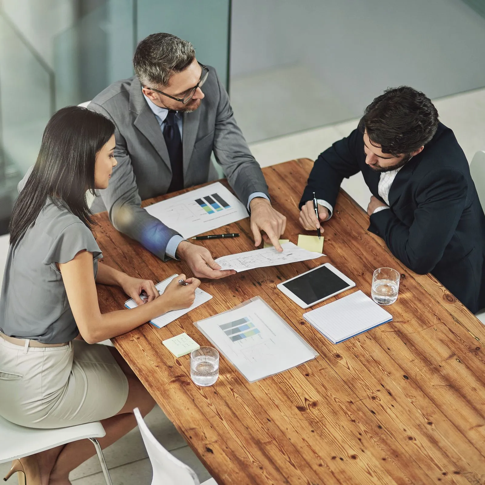 Three businesspeople reviewing charts and documents together at a wooden conference table.