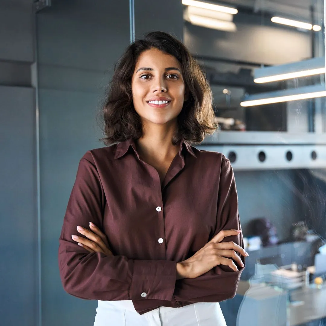 Confident young woman with crossed arms smiling in a modern office setting.