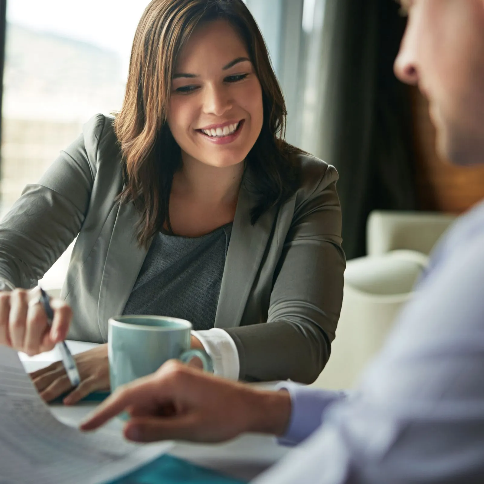 Smiling businesswoman reviewing documents with a colleague at a table with a coffee cup.
