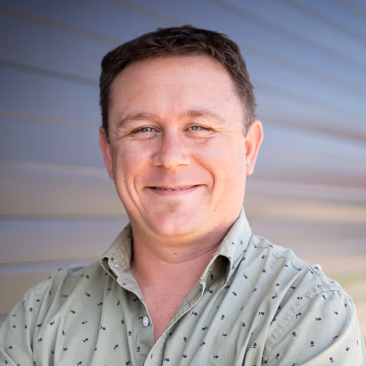 Smiling man with short brown hair wearing a light green shirt with small floral patterns.