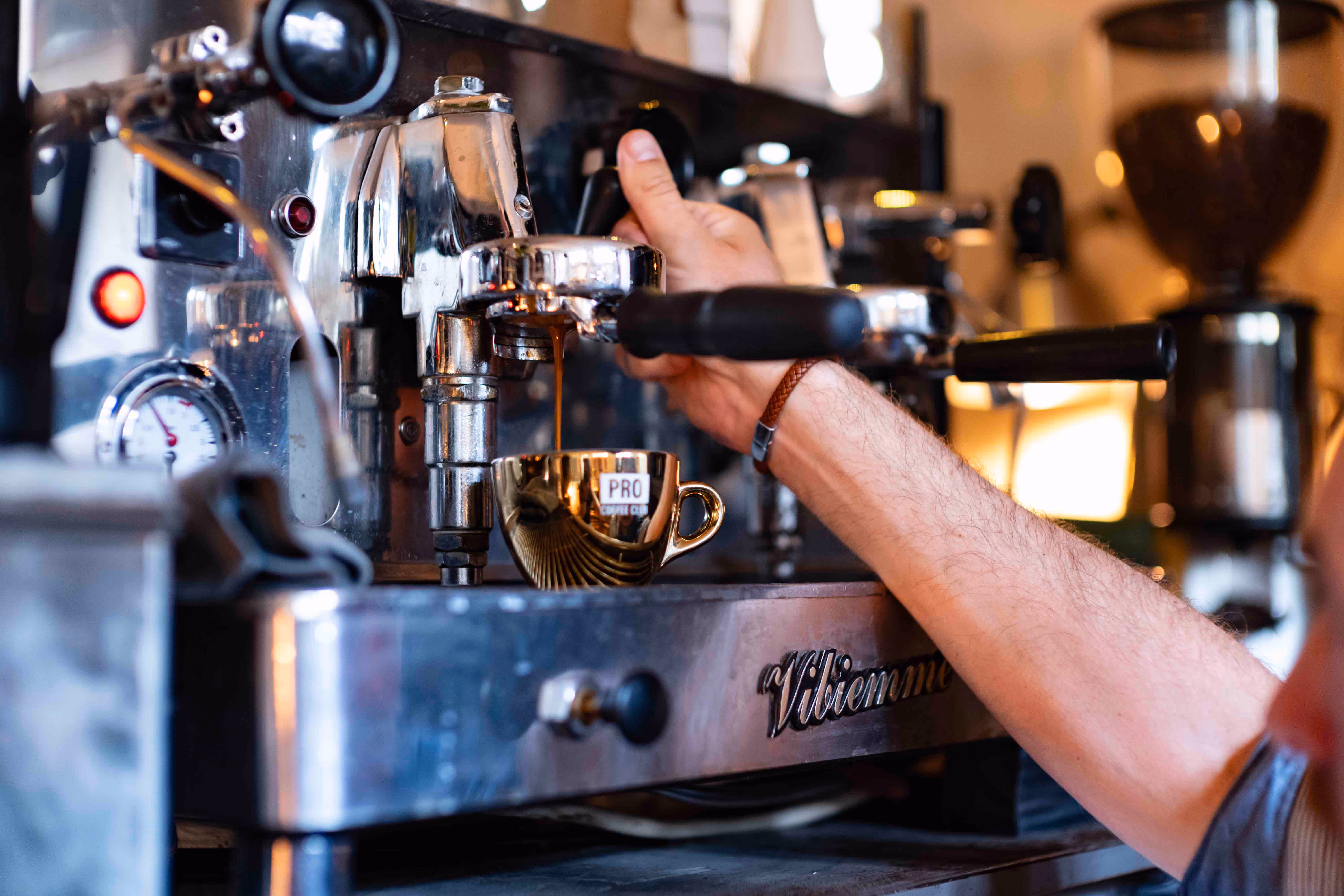Hand bedient een professionele espressomachine waarbij koffie in een gouden cappuccino-kopje loopt.