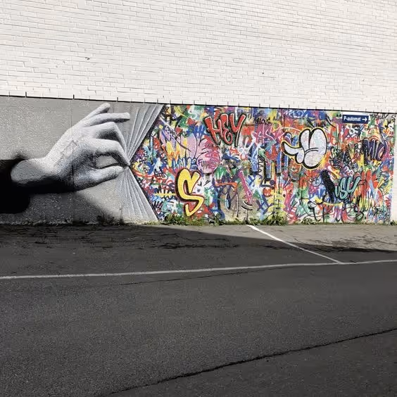 Muurkunst met een zwart-witte hand die een kleurrijk graffiti-gordijn op een bakstenen muur opent.