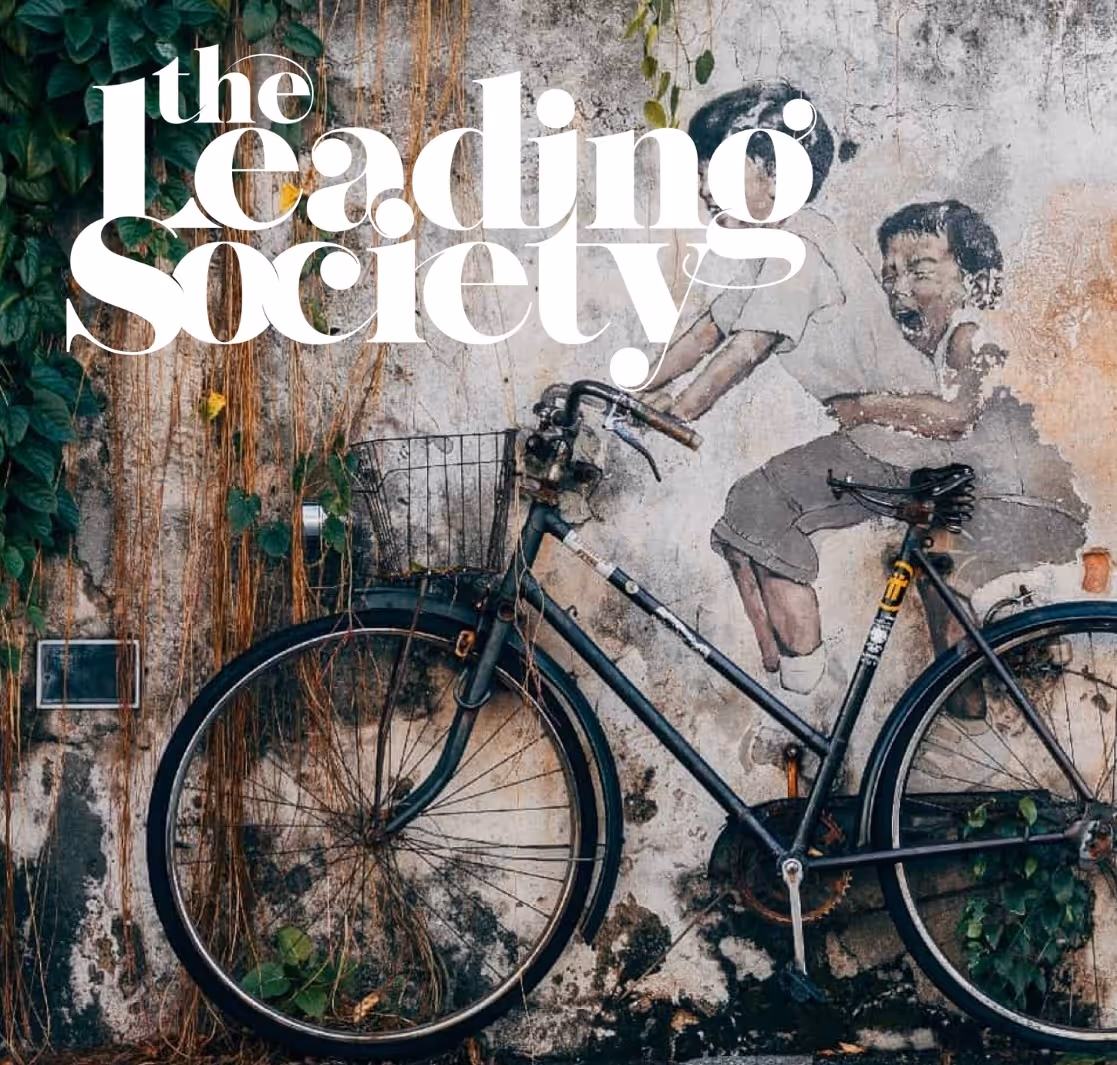 Muurschildering van twee kinderen op een fiets, omringd door klimop op een verweerde muur met de tekst 'the leading Society'.
