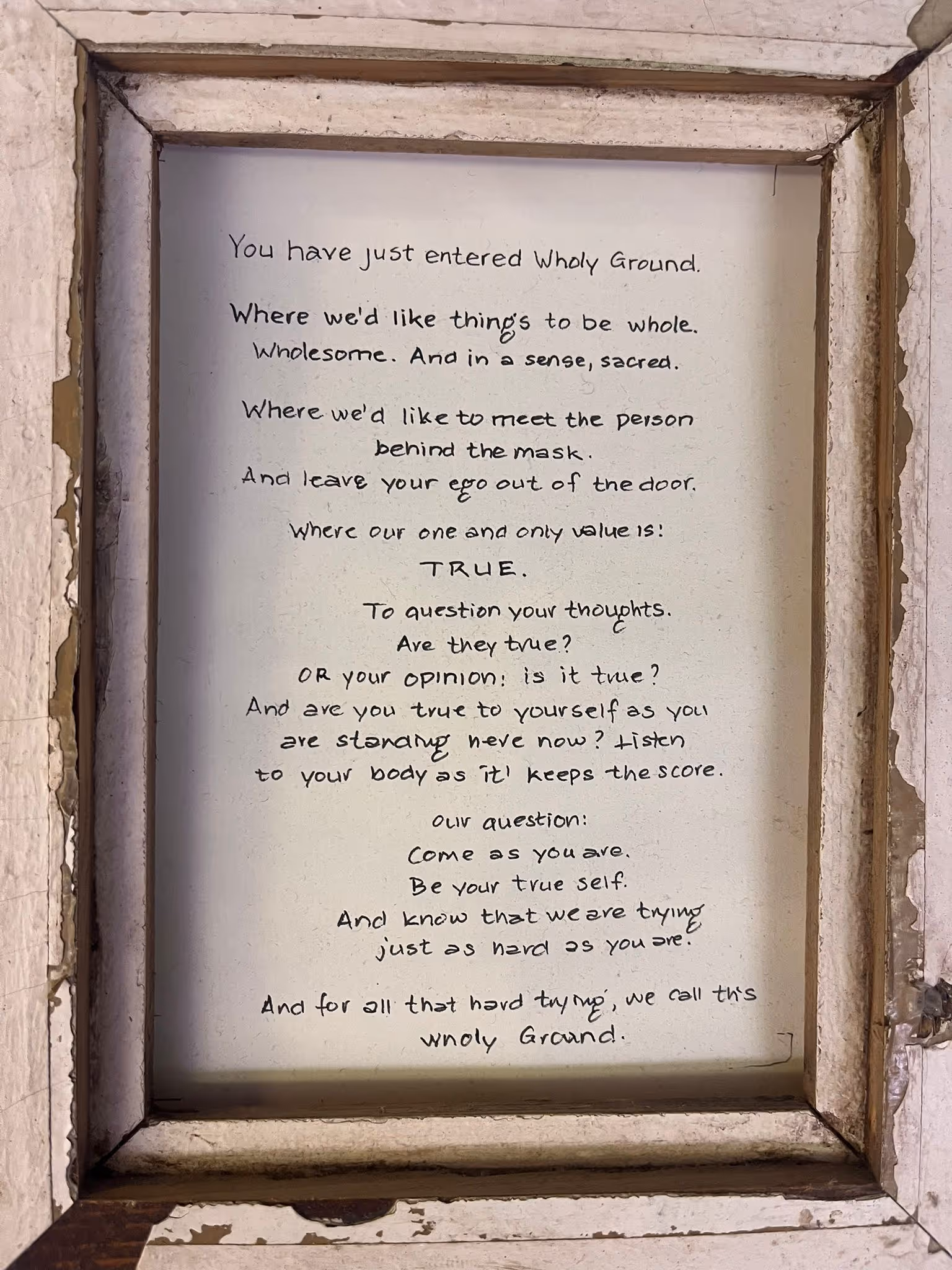 In een versleten houten lijst hangt een handgeschreven tekst met de titel 'Wholy Ground', die oproept tot waarheidsgetrouwheid, echtheid en het achterlaten van ego bij binnenkomst.