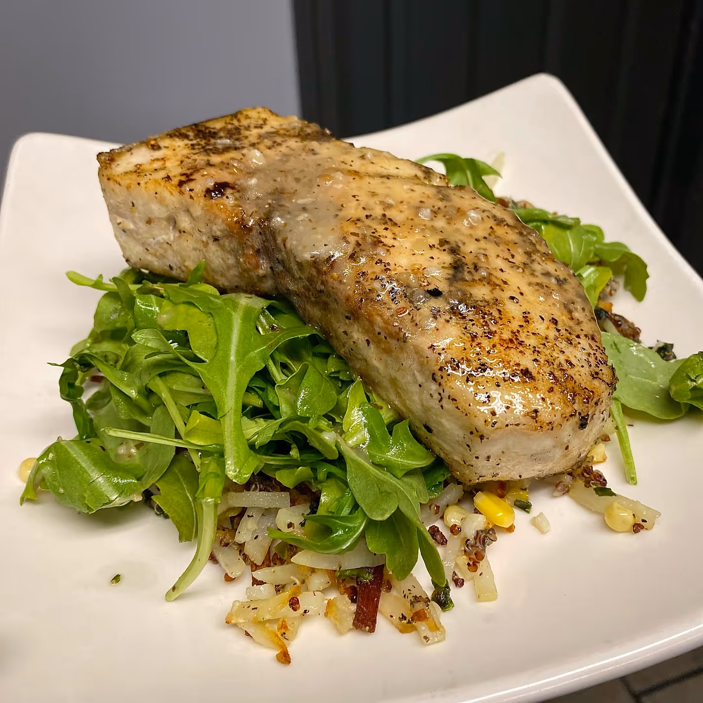 Grilled swordfish on a bed of arugula and seasoned quinoa hash, garnished with herbs.