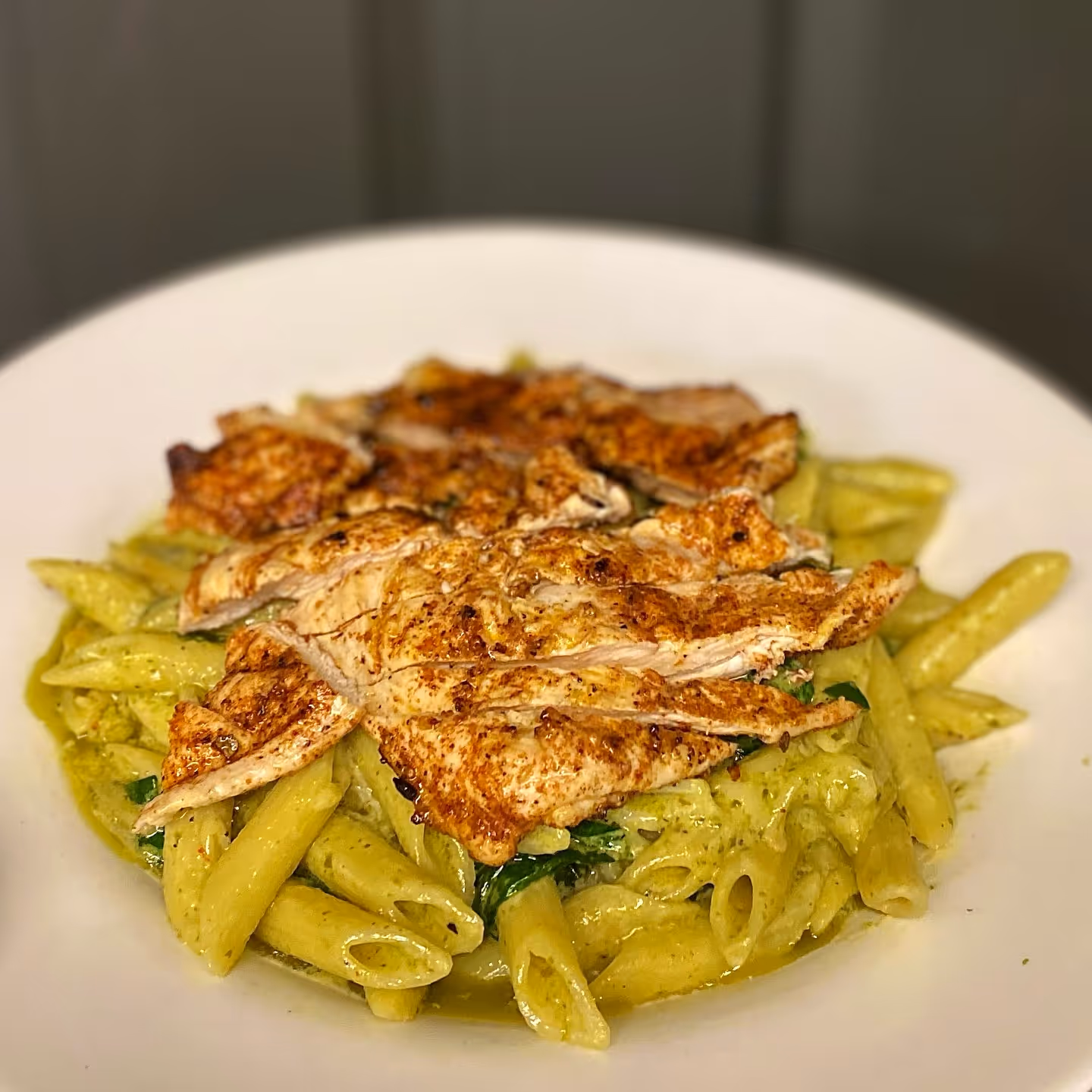 Pesto Penne Pasta with blackened chicken, sun-dried tomatoes, and spinach.