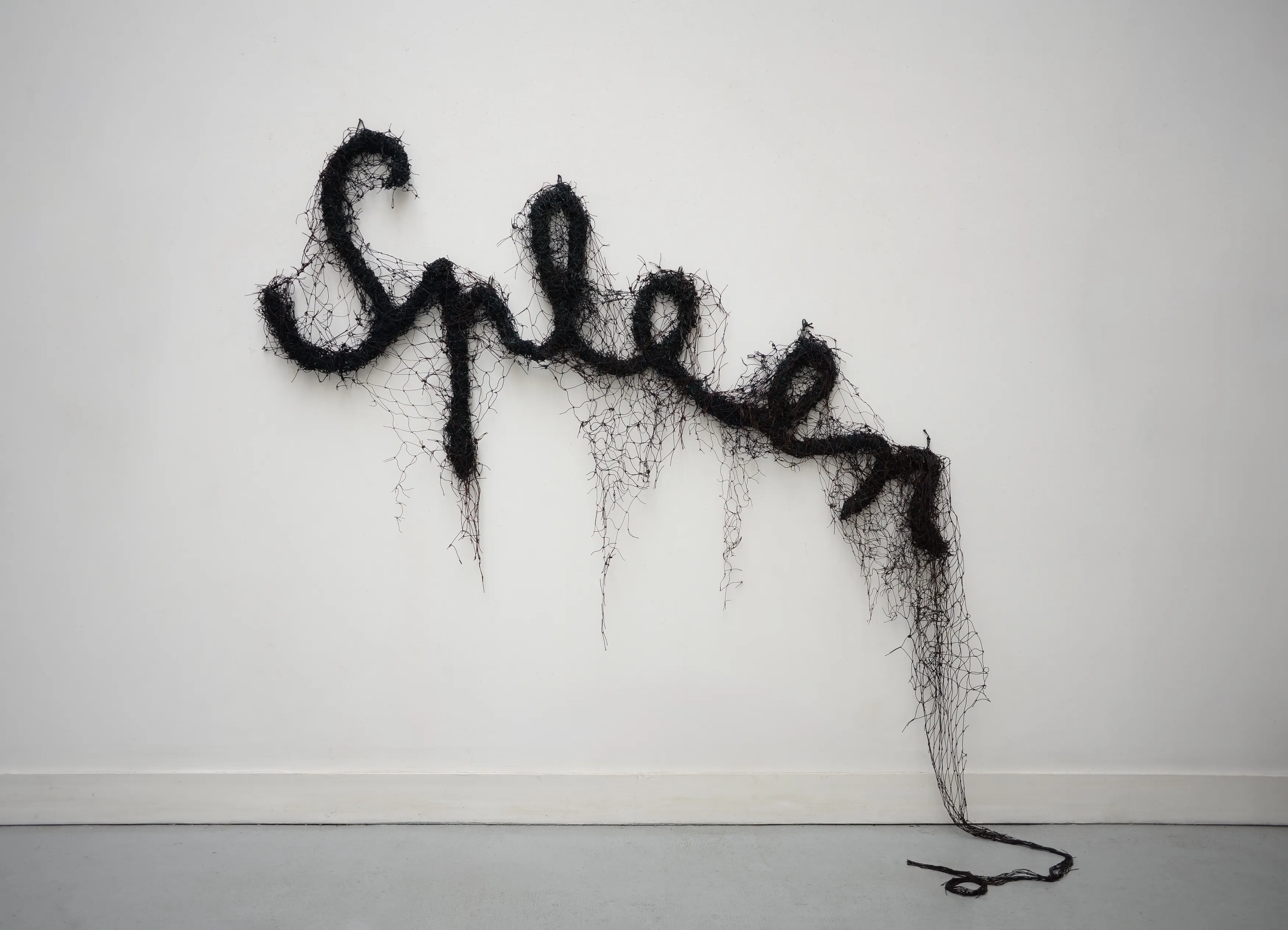 Pinned at the tops of its letters, the word remains legible while the net sags toward the floor. Image Credit: Annette Messager, Spleen, 2025. Photo: Rebecca Fanuele.