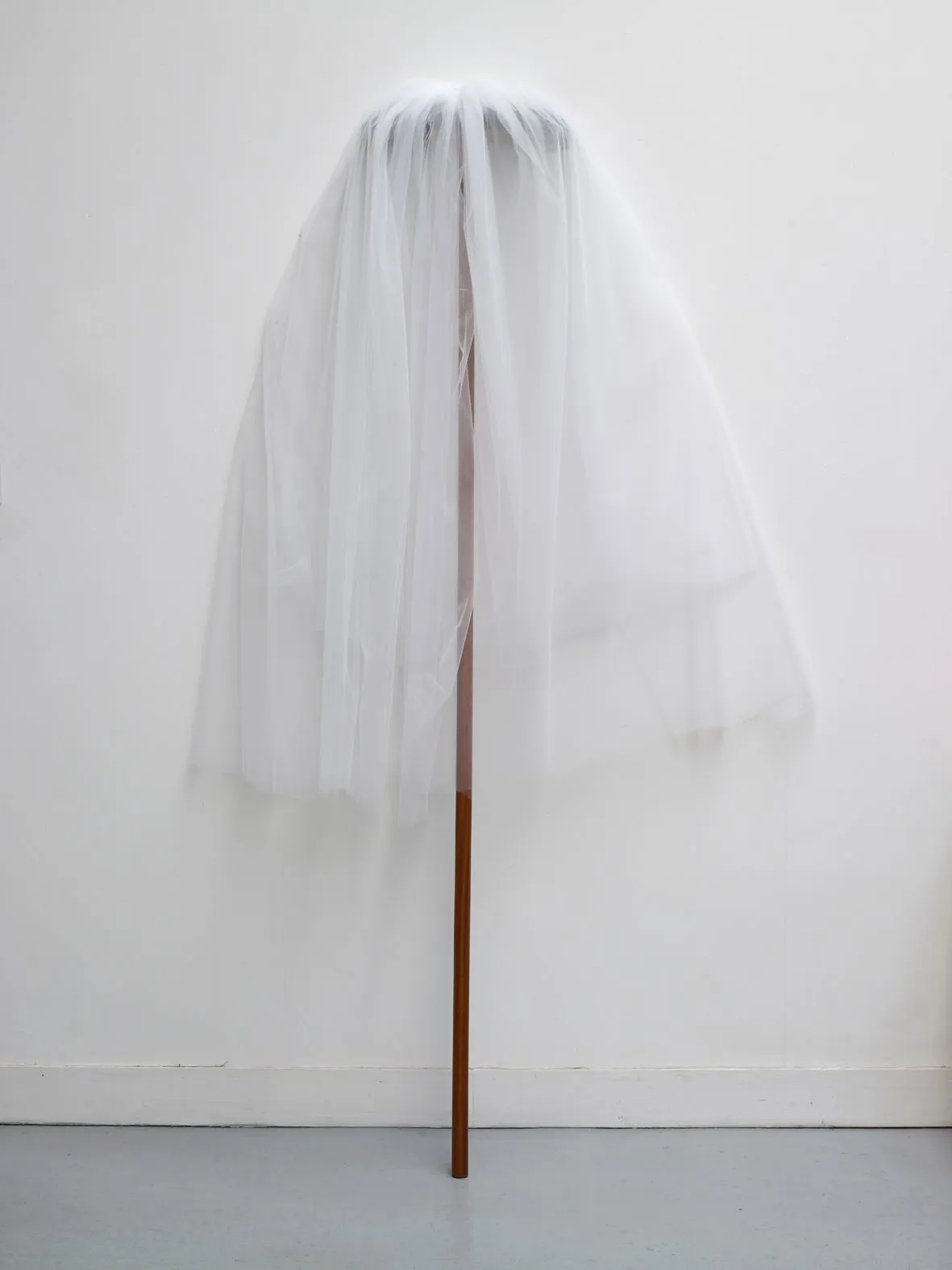 A bridal veil announces an absent body while the upturned broom beneath it leans against the wall for support. Image Credit: Annette Messager, Just Married, 2011. Photo: Rebecca Fanuele.