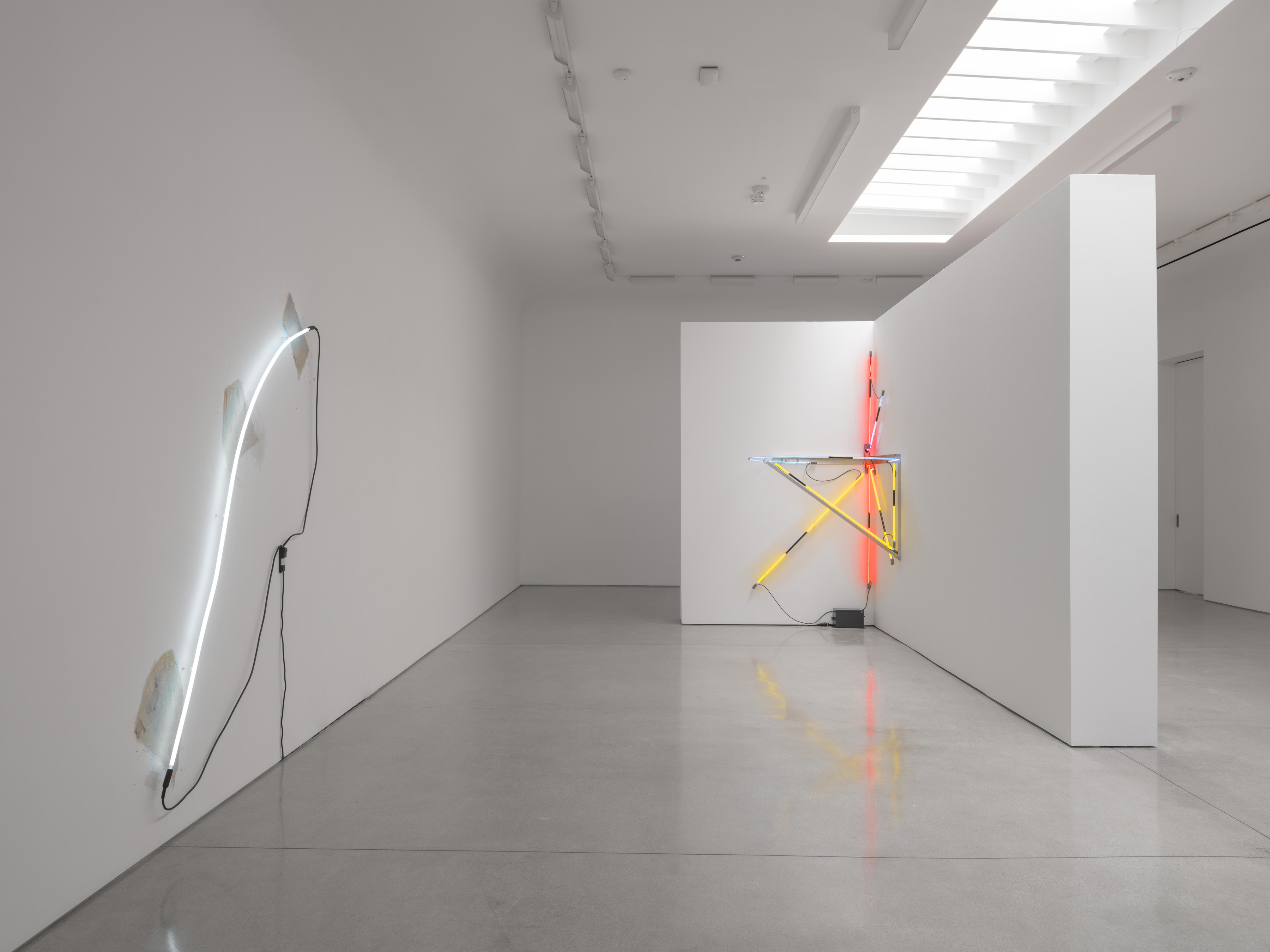 Past the mouth of the bay, Arced Neon (Cool White) rises over three torn sheets; both cables meet at a small unit on the wall. Image Credit: Installation view. Courtesy Estate of Keith Sonnier and David Kordansky Gallery. Photo: Jeff McLane.