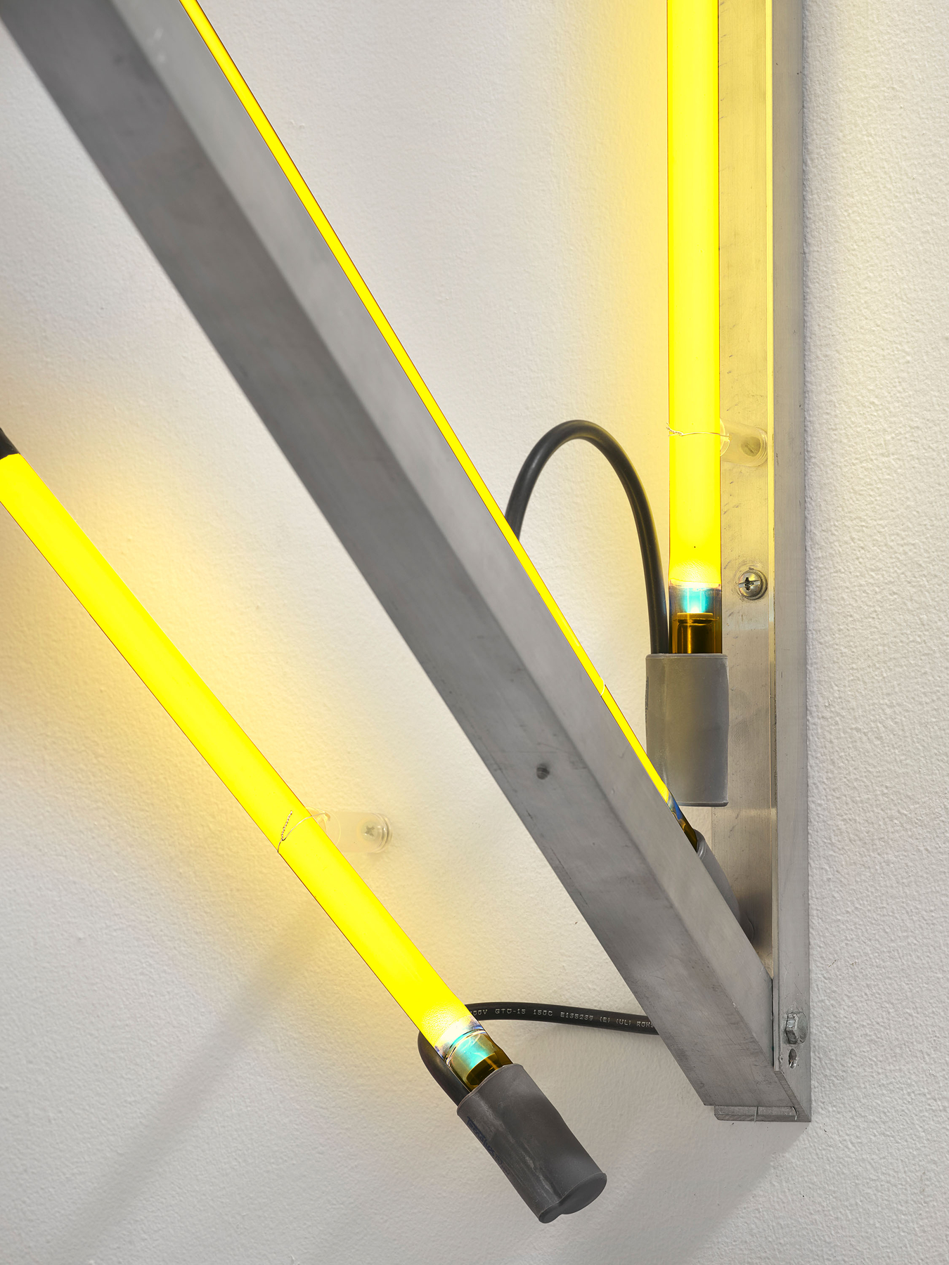 The aluminum diagonal is screwed to a short vertical angle, a tube in its channel. Every end sits in a grey housing. Image Credit: Untitled Neon Corner Piece, 1969 (detail). Courtesy Estate of Keith Sonnier and David Kordansky Gallery. Photo: Jeff McLane.