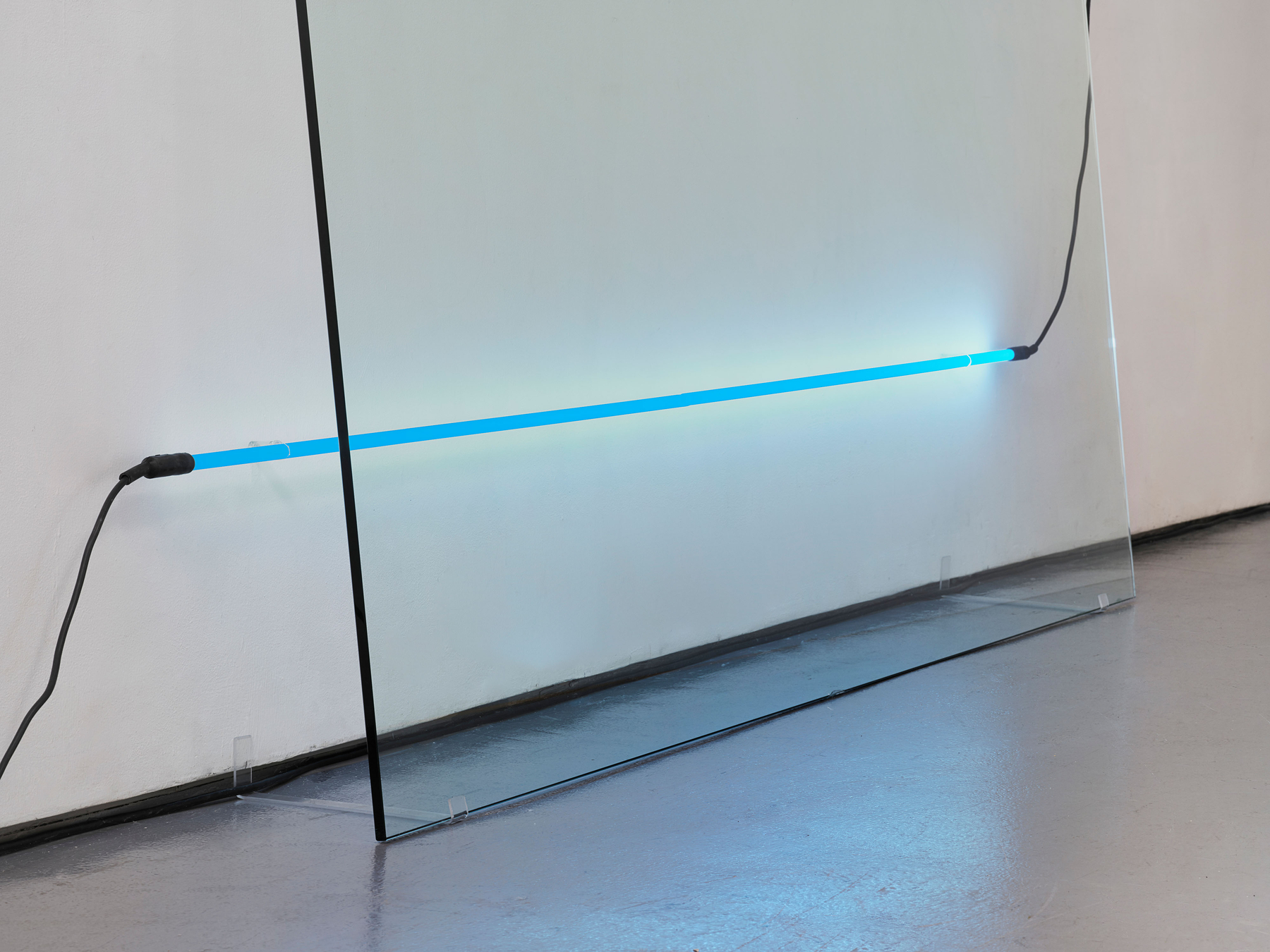 The lowest tube runs past the glass, its left cap out on open wall. The pane stands on clear pads, its base well off the wall. Image Credit: Ba-O-Ba I, 1969 (detail). Courtesy Estate of Keith Sonnier and David Kordansky Gallery. Photo: Jeff McLane.