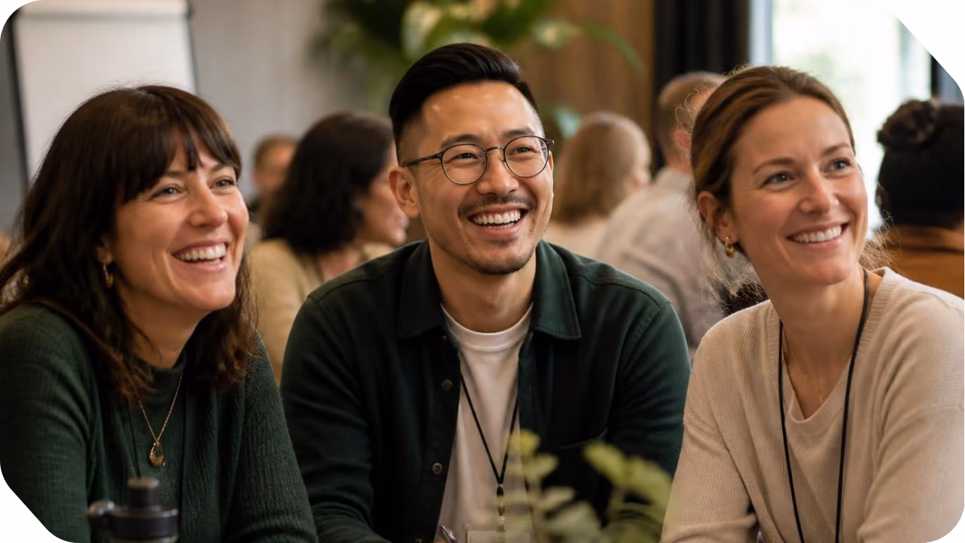 Three diverse people smiling and sitting together in a social or work setting with blurred background.