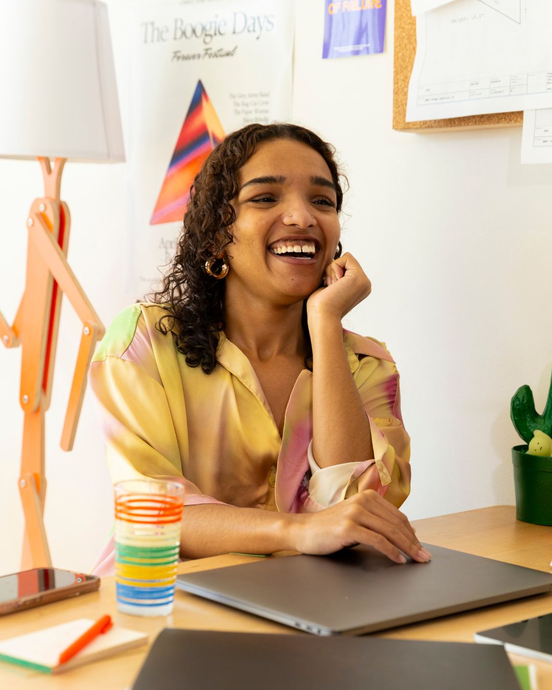 Smiling woman in colorful shirt sitting at desk with closed laptop and colorful striped glass.