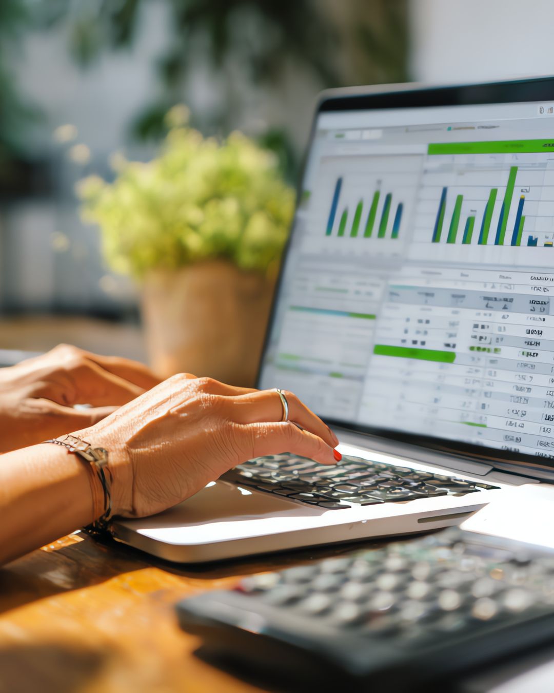 Person working on laptop displaying financial charts and data with a calculator nearby on wooden desk.