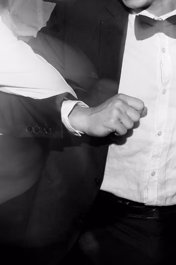 Close-up of a man in a tuxedo with a bow tie, flexing his right arm.