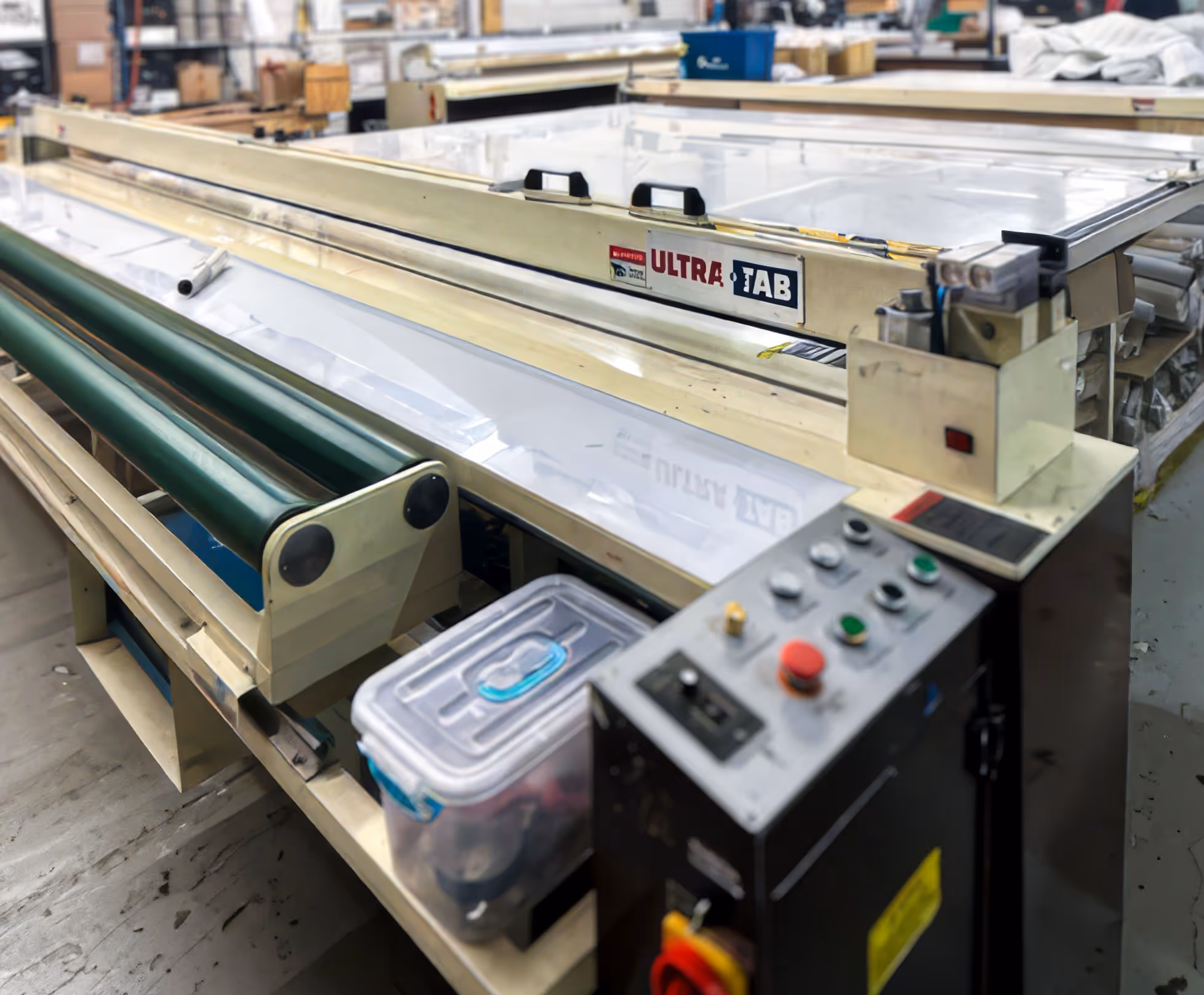 Industrial fabric cutting machine labeled Ultra Tab in a workshop with control panel and green rollers.