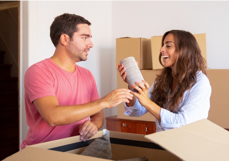 Ein Mann und eine Frau packen gemeinsam Kartons aus und lachen dabei.