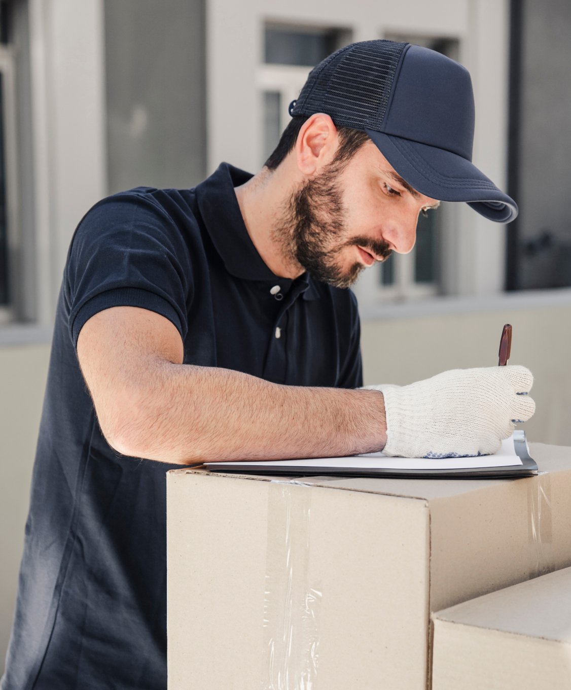 Ein Mann mit schwarzer Kappe und weißen Handschuhen unterschreibt ein Dokument auf einem Karton.