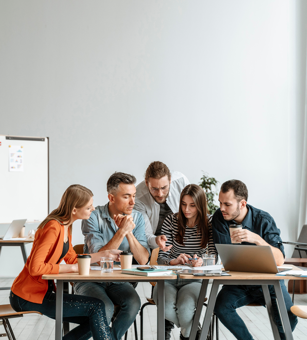 Five colleagues having a meeting, reviewing documents and using a laptop at a wooden table.