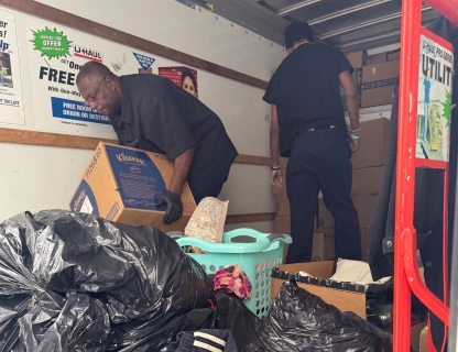 Two men loading boxes and bags of belongings into the back of a moving truck.