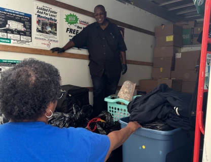 A man and a woman with moving boxes and storage bins inside a moving truck.