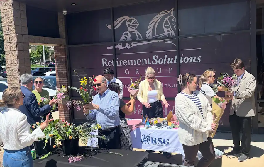 Group of people arranging flowers outside Retirement Solutions Group office on a sunny day.