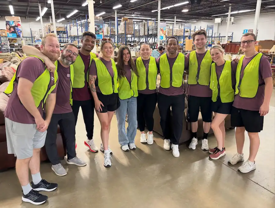 Group of volunteers wearing yellow safety vests posing together inside a warehouse with shelves.