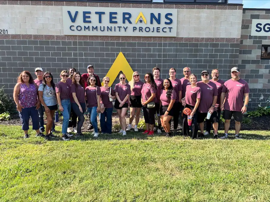 Group of volunteers standing in front of Veterans Community Project building on grass.