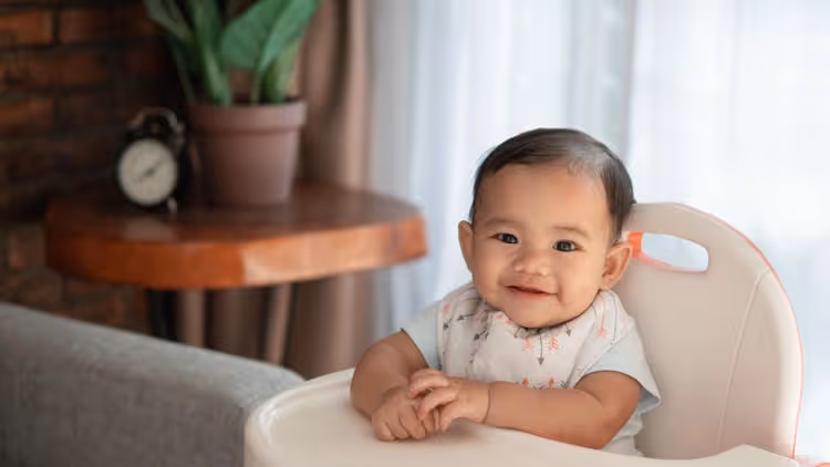 A baby in a baby chair smiling just before mealtime