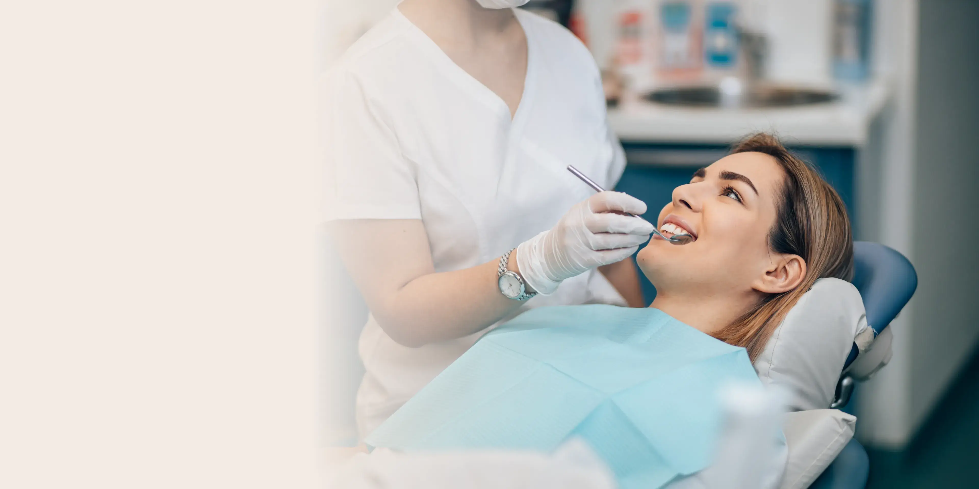 Dentist wearing gloves and a mask examining a smiling woman reclining in a dental chair with a blue bib.